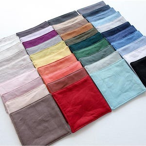 Könnte beinhalten: Eine Sammlung quadratischer Stoffuntersetzer, die in einem Raster angeordnet sind und eine Vielzahl von Volltonfarben wie Weiß, Schwarz, Rot, Blau, Grün, Gelb, Rosa, Lila, Braun und Grau aufweisen, jeweils mit genähten Kanten und glatter Textur.
