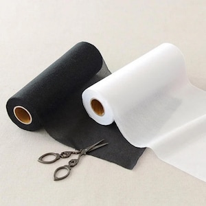 May include: Two rolls of fabric, one black and one white, are displayed. The black fabric is a textured material, while the white fabric appears more sheer. A pair of vintage scissors rests on the black fabric.