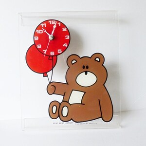May include: A clear acrylic clock with a brown bear holding two red balloons. The clock face is red with white numbers and hands. The clock reads "BOO BOO BEAR" and "1985 GOLDEN MESA, INC. U.S.A."