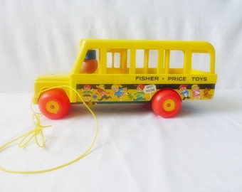 May include: A vintage yellow Fisher-Price toy school bus with red wheels and a yellow pull string. The bus features a colorful illustration of children and the text "Fisher-Price Toys". A small orange figure is visible inside the bus.