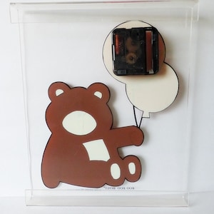 May include: A brown teddy bear holding two white balloons. The clock mechanism is visible on the back of the clock.
