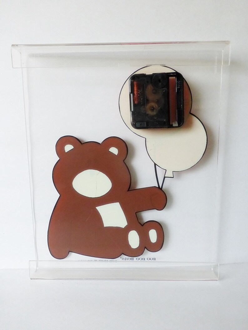 May include: A brown teddy bear holding two white balloons. The clock mechanism is visible on the back of the clock.