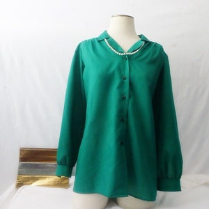 May include: A green long-sleeved button-down shirt with a collared neckline. The shirt is on a mannequin and has a pearl necklace draped over the collar.