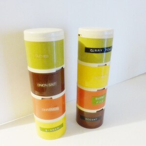 Könnte beinhalten: Satz von vier stapelbaren Gewürzgläsern mit Etiketten für Nelken, Zwiebelsalz, Paprika, Ingwer, Currypulver, Gumbo-Datei und Akzent. Die Gläser sind gelb, orange, braun und grün.