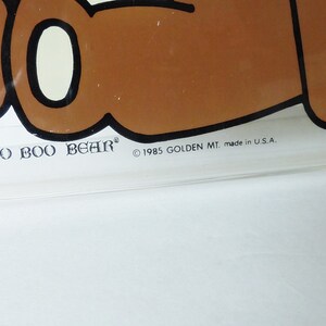 May include: A clear plastic Boo Boo Bear lunchbox with a brown bear cartoon illustration. The lunchbox has the text "Boo Boo Bear" and "&copy; 1985 GOLDEN MT. made in U.S.A."