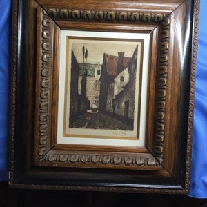 May include: A framed black and white print of a street scene with buildings and a cobblestone street. The print is signed "Milan Creg" in the bottom right corner.