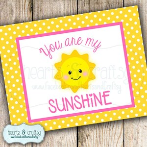 Pu&ograve; includere: Un biglietto giallo con pois bianchi e un bordo rosa. Il biglietto dice "Sei il mio sole" con un sole giallo sorridente al centro.