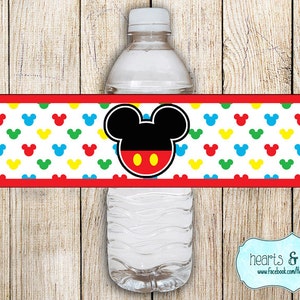 May include: Water bottle label featuring Mickey Mouse with red, yellow, blue, and green Mickey Mouse ears on a white background. The label has a red border and the text "hearts & crafty" is visible at the bottom.