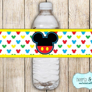 May include: Water bottle label featuring Mickey Mouse with red, yellow, blue, and green polka dots. The label has a yellow border and the text "hearts & crafty" with a website address.