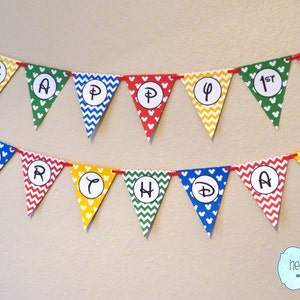 K&ouml;nnte beinhalten: Ein farbenfrohes Banner mit Mickey-Maus-Ohren und den Worten "Happy 1st Birthday" in wei&szlig;en Kreisen. Das Banner besteht aus roten, gelben, gr&uuml;nen und blauen Dreiecken mit wei&szlig;en Punkten und wei&szlig;en Mickey-Maus-Ohren.