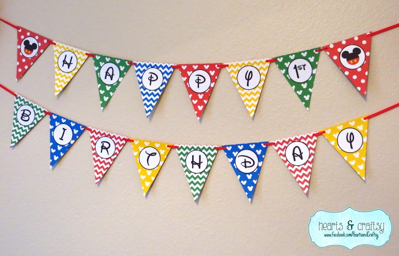 K&ouml;nnte beinhalten: Ein farbenfrohes Banner mit Mickey-Maus-Ohren und den Worten "Happy 1st Birthday" in wei&szlig;en Kreisen. Das Banner besteht aus roten, gelben, gr&uuml;nen und blauen Dreiecken mit wei&szlig;en Punkten und wei&szlig;en Mickey-Maus-Ohren.