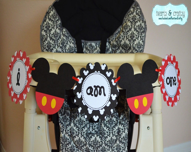 May include: A Mickey Mouse themed first birthday banner with red, black and white scalloped circles. The banner reads "I am one".