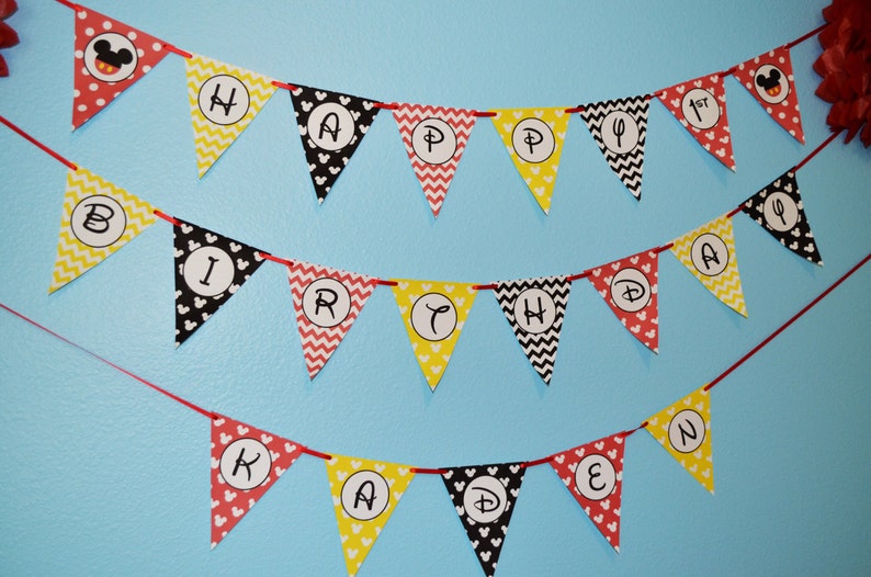 May include: A red, yellow, and black Mickey Mouse themed banner with the words "Happy 1st Birthday Kaden".