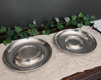 Pode incluir: Dois pratos de servir prateados com um centro elevado, sobre uma toalha de mesa branca em uma mesa de madeira.