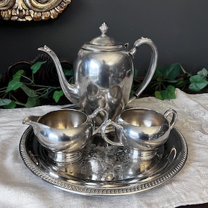 May include: A silver tea set with a teapot, creamer, and sugar bowl on a silver tray. The set has a classic design with ornate details.