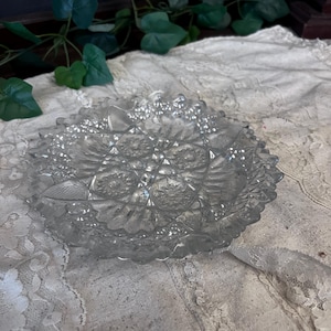 May include: A clear glass dish with a decorative, cut-glass pattern. The dish has a scalloped edge and is ideal for serving snacks or desserts.