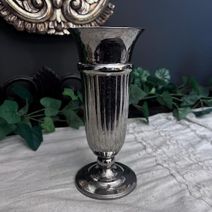 以下が含まれることがあります： フレアトップと丸いベースを備えた、シルバー調の溝付き花瓶。 花瓶は反射面とクラシックでエレガントなデザインです。 花瓶は、花を飾ったり、装飾的なアクセントとして使用するのに適しています。