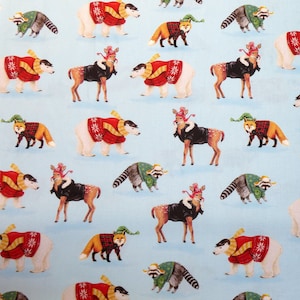 Puede incluir: Una tela azul claro con un patrón repetido de animales festivos. El diseño incluye ciervos, zorros, mapaches y osos polares, cada uno adornado con ropa de invierno como suéteres y sombreros, creando un tema navideño caprichoso.