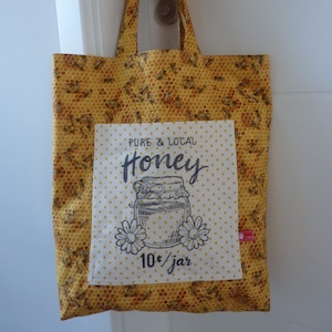 May include: A yellow tote bag with a honeycomb pattern and a white patch that says "Pure & Local Honey" with a drawing of a honey jar and the text "10¢/jar".