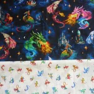 Op de afbeelding: Een stofprint met twee verschillende secties. Het bovenste gedeelte toont een donkerblauwe nachtelijke hemel vol kleurrijke draken, kastelen en sterren. Het onderste gedeelte toont een witte achtergrond met een patroon van kleine, herhalende draken.