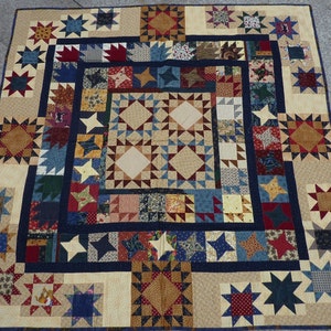 Può includere: Una trapunta con un design a patchwork che presenta una varietà di tessuti in tonalità di blu, rosso, marrone e crema. La trapunta è composta da un quadrato centrale circondato da un bordo di stelle e altre forme geometriche.