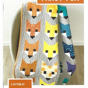 May include: A quilt pattern featuring a repeating design of stylized fox faces in various colors, including orange, yellow, and blue, set against a gray background. The text "FANCY FOX" is at the top. The pattern is by Elizabeth Hartman.