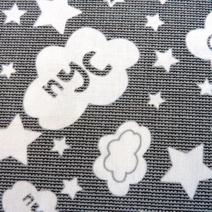 Könnte beinhalten: Weißer Stoff mit grauem Hintergrund, der ein sich wiederholendes Muster aus Sternen und Wolken zeigt. Die Wolken haben das Wort "NYC" darin geschrieben.