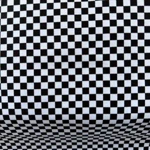 Könnte beinhalten: Nahaufnahme eines Stoffes mit einem schwarz-weißen Schachbrettmuster. Das Muster besteht aus gleichmäßig verteilten schwarzen Quadraten auf weißem Hintergrund. Der Stoff ist leicht gewölbt, wodurch ein Gefühl von Tiefe entsteht.