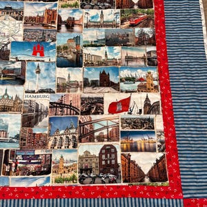 May include: A patchwork quilt with postcard images of Hamburg, Germany. The quilt has a red border with white anchors and a blue and white striped backing. The postcards show various landmarks and scenes from the city.