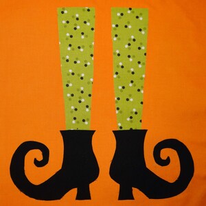 Könnte beinhalten: Orangefarbener Hintergrund mit einem Halloween-Motiv. Das Bild zeigt ein Paar schwarze Hexenschuhe mit gebogenen Zehen und grüne Beine mit weißen und schwarzen Tupfen. Das Design ist einfach und auffällig.