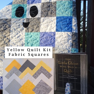 May include: A patchwork quilt with a smiling face design, featuring squares of white, blue, gray, and teal. The image also shows a book titled "The Little Ghost Who Was a Quilt" and a display of yellow quilt kit fabric squares.