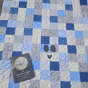 May include: A handmade quilt with a patchwork design in shades of blue, gray, and white. The quilt features a ghost face design and a book titled "The Little Ghost Quilts Winter Surprise."