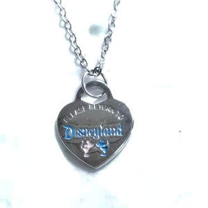 May include: Silver heart-shaped necklace with a chain. The pendant has the words "Please Return to Disneyland" engraved on it with a blue and pink Mickey Mouse and Minnie Mouse design.