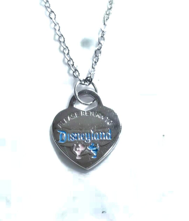 May include: Silver heart-shaped necklace with a chain. The pendant has the words "Please Return to Disneyland" engraved on it with a blue and pink Mickey Mouse and Minnie Mouse design.