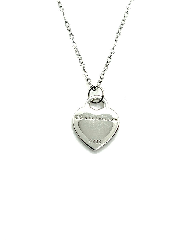May include: Silver heart pendant necklace with a chain. The back of the pendant has the text "&copy;Disneyland.com" and the number "925".