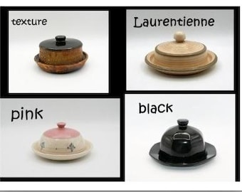 Puede incluir: Un collage de cuatro mantequilleras con tapa. Arriba a la izquierda, etiquetada como texture, una mantequillera marrón con tapa negra. Arriba a la derecha, etiquetada como Laurentienne, una mantequillera en tono madera claro. Abajo a la izquierda, etiquetada como pink, una mantequillera rosa y crema. Abajo a la derecha, etiquetada como black, una mantequillera negra sólida.