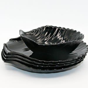 Può includere: Una pila di quattro piatti in ceramica nera lucida con una distinta forma a foglia. Ogni piatto presenta una superficie strutturata che imita le venature di una foglia e un bordo smerlato e ondulato che segue il contorno organico.