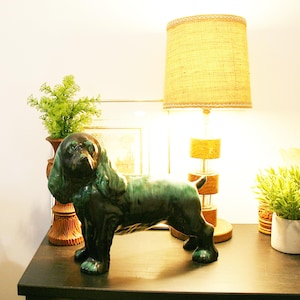 May include: A glossy ceramic dog figurine featuring a deep emerald green and black glaze. The canine sculpture stands in a profile position with long, textured ears and a smooth, reflective finish, showcasing a rich color gradient throughout.
