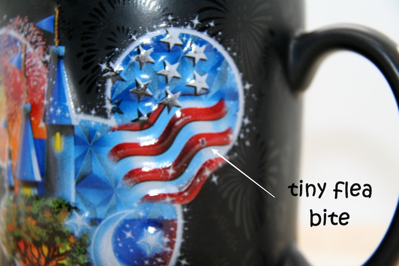 May include: Black ceramic mug with a patriotic design featuring a stylized American flag, stars, and a blue castle. The mug has a black handle and a small imperfection. The mug is decorated with fireworks.