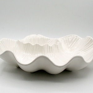 May include: A white ceramic serving bowl with a wavy, seashell-like design. The bowl has a glossy finish and a textured interior, perfect for serving salads or displaying decorative items. The bowl is a decorative piece.