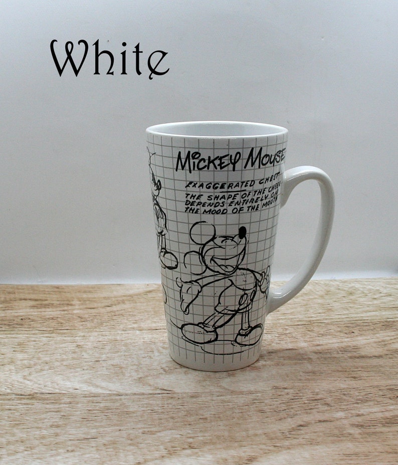 May include: White ceramic Mickey Mouse mug with a black and white sketch design. The mug features the text "MICKEY MOUSE" and a quote about the character's chest and mood. The mug has a tall, slender shape and a curved handle.