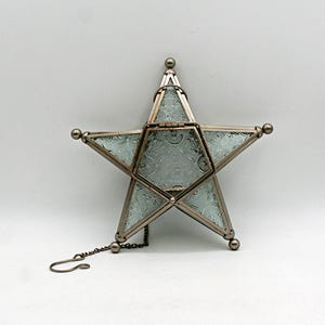 Peut inclure: Un récipient en forme d'étoile composé de verre texturé et de métal avec une finition métallique. L'objet présente des panneaux de verre à motifs, une ouverture à charnière sur le dessus et une petite chaîne métallique avec un crochet.