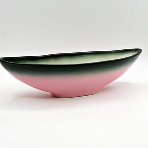 May include: An elongated ceramic bowl with a boat-like shape, featuring a smooth matte finish. The exterior transitions from a soft pastel pink at the base to a dark charcoal grey rim, while the interior displays a light cream colour.