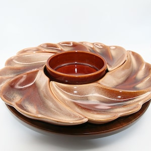 May include: A vintage serving dish with a central bowl and six petal-shaped compartments. The dish has a glossy, two-tone brown glaze and sits on a dark wooden base. Suitable for serving snacks or appetizers.
