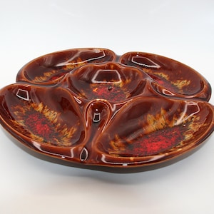 Peut inclure: Un plat de service divisé en céramique marron vintage avec une finition brillante. Le plat comporte un compartiment central et quatre sections environnantes, chacune avec un motif tacheté rouge et or. Idéal pour servir des collations ou des apéritifs.