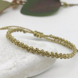 May include: A gold braided friendship bracelet with a sliding knot closure.