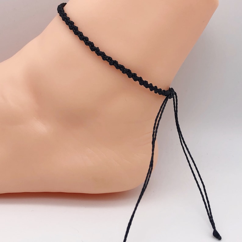 Puede incluir: Un brazalete de tobillo trenzado negro con lazos ajustables.