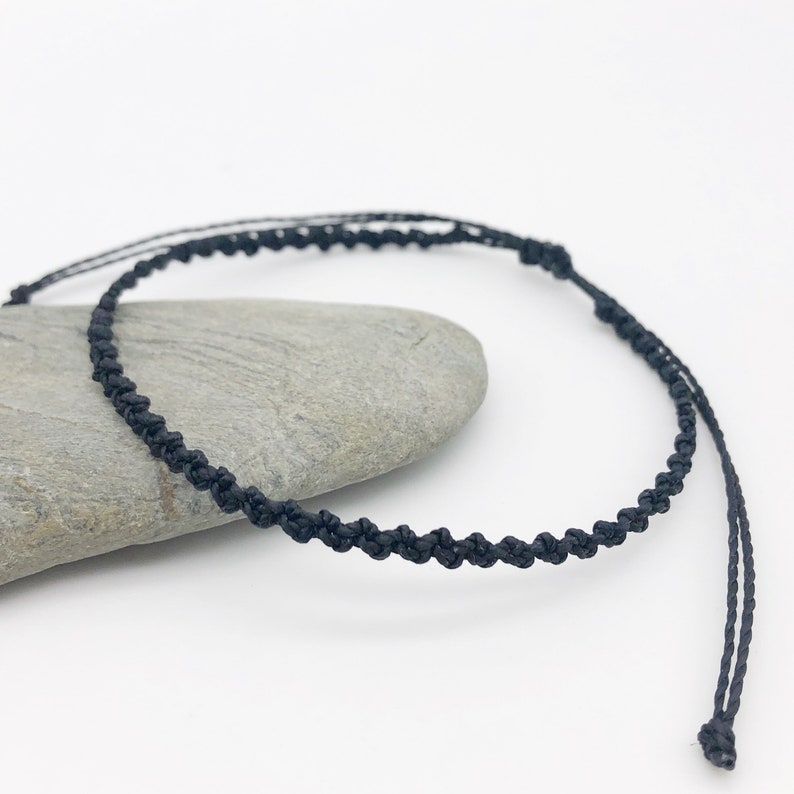 Puede incluir: Un brazalete sencillo de cord&oacute;n trenzado negro. El brazalete est&aacute; hecho de un cord&oacute;n fino y negro que se trenza para crear un look delicado y elegante.