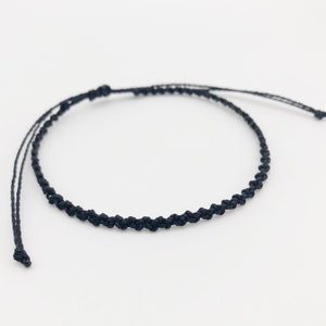 Puede incluir: Un brazalete trenzado negro simple con cierre de nudo deslizante.