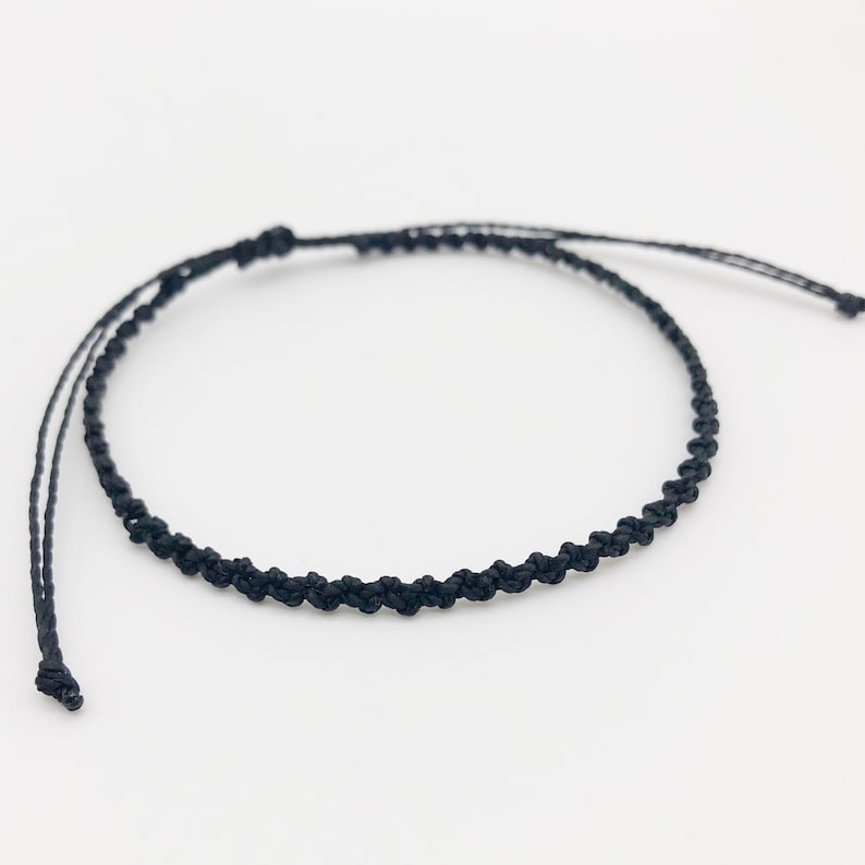 Puede incluir: Un brazalete trenzado negro simple con cierre de nudo deslizante.
